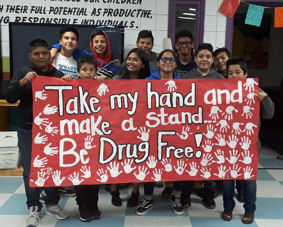 kids holding a painted sign that says "take my hand and make a stand, be drug free!"
